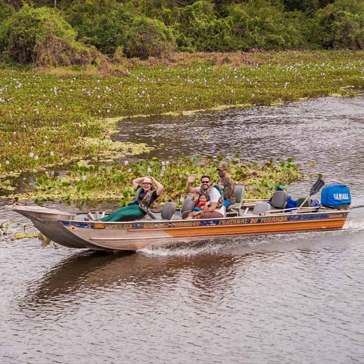 Pessoas em um barco navegando por um rio cercado por vegetação aquática e flores, em um ambiente natural exuberante.