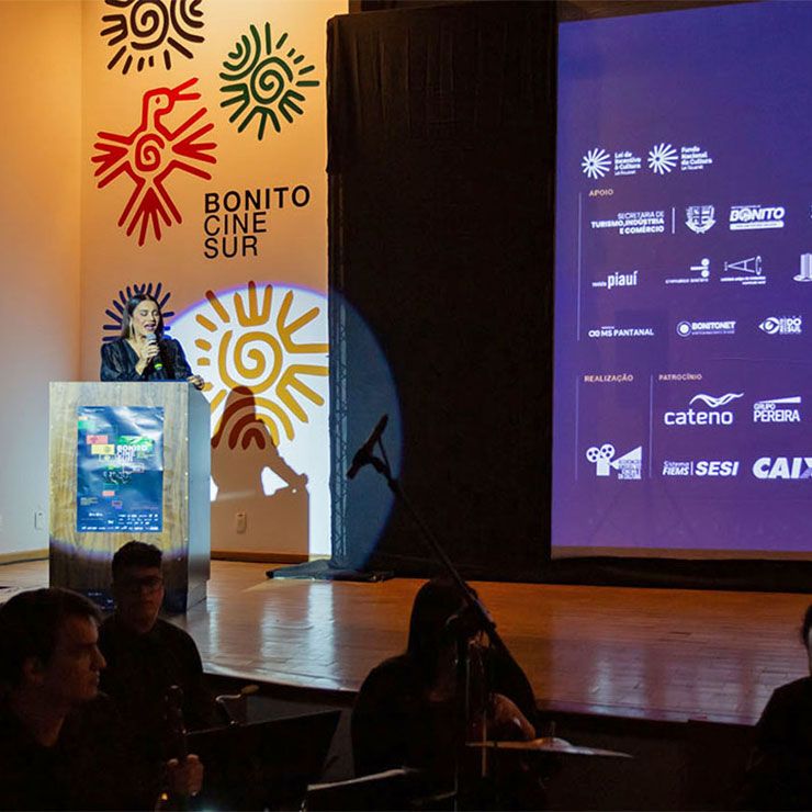 Mulher em um pódio discursando no evento "Bonito Cine Sur", com logos e patrocinadores ao fundo.